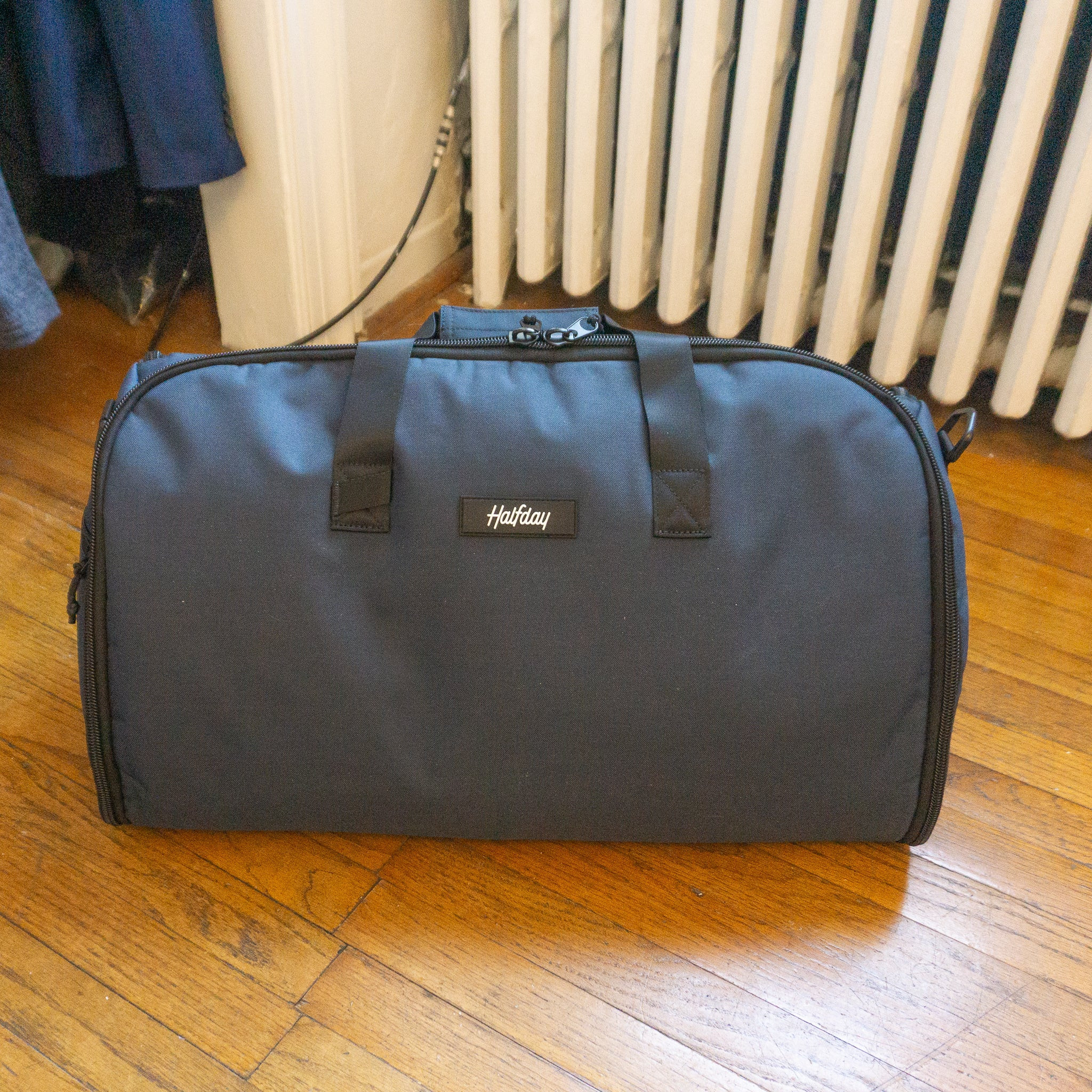 Halfday Garment Duffel bag in a neutral color, placed on a light wooden floor, showcasing its duffel shape.