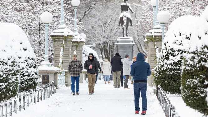 A general view showing people walking through a snow-covered Boston Public Garden, depicting typical winter conditions in the Northeast during the holiday season.