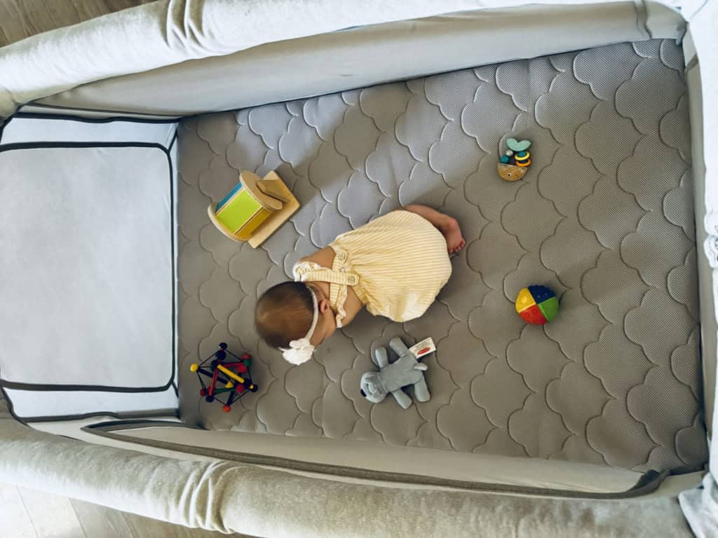 Baby enjoying playtime in a spacious Newton Travel Crib play yard with toys, demonstrating its use as a safe and comfortable play space.