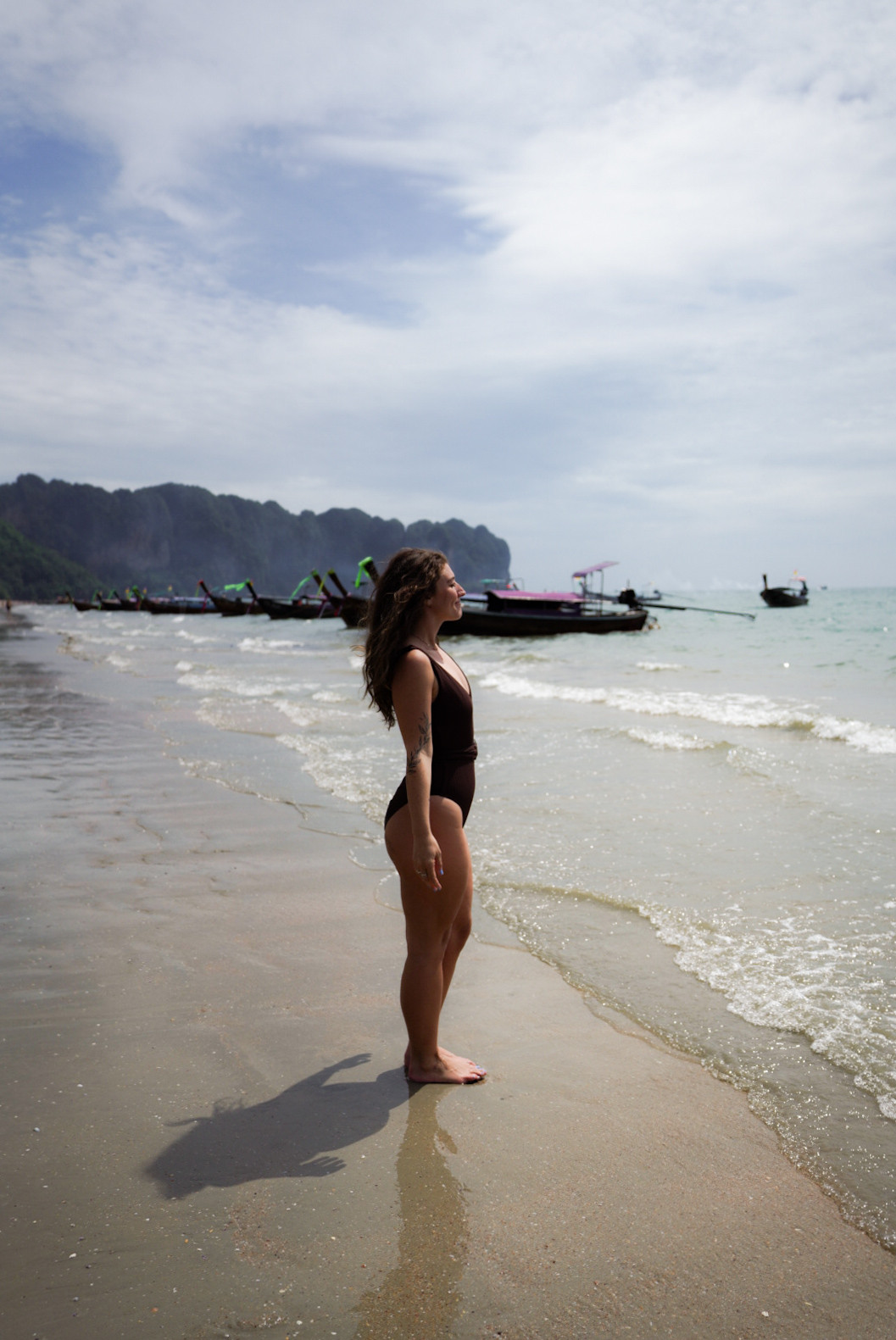 Tourists relaxing on Ao Nang Beach, Krabi, Thailand, with clear blue water and longtail boats in the background.