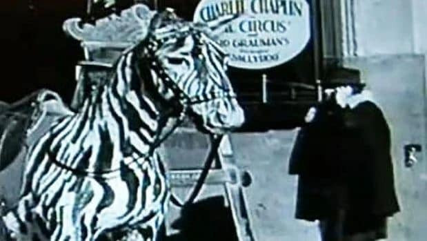 Still from Charlie Chaplin movie footage showing a woman with a device resembling a cell phone