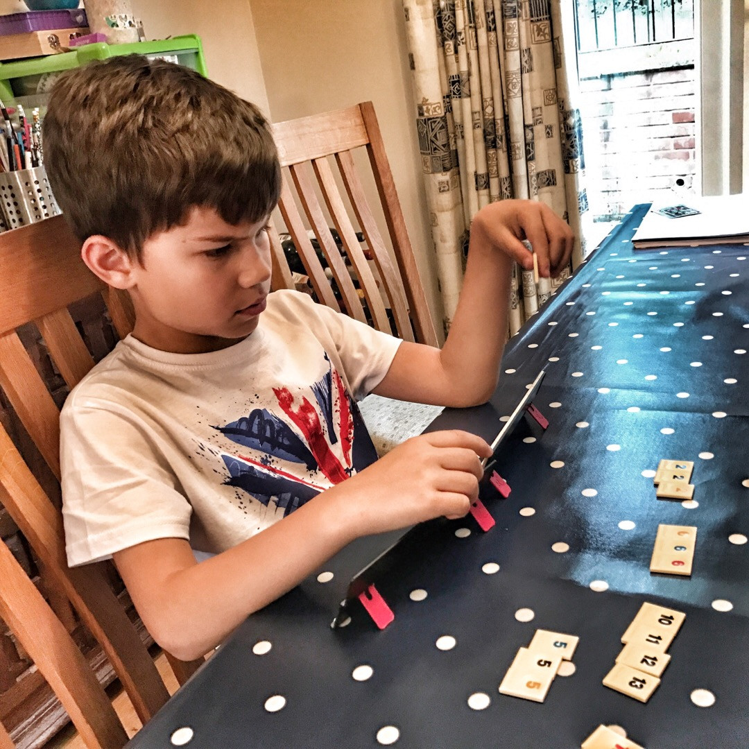 A young child playing Rummikub Travel Set on a table