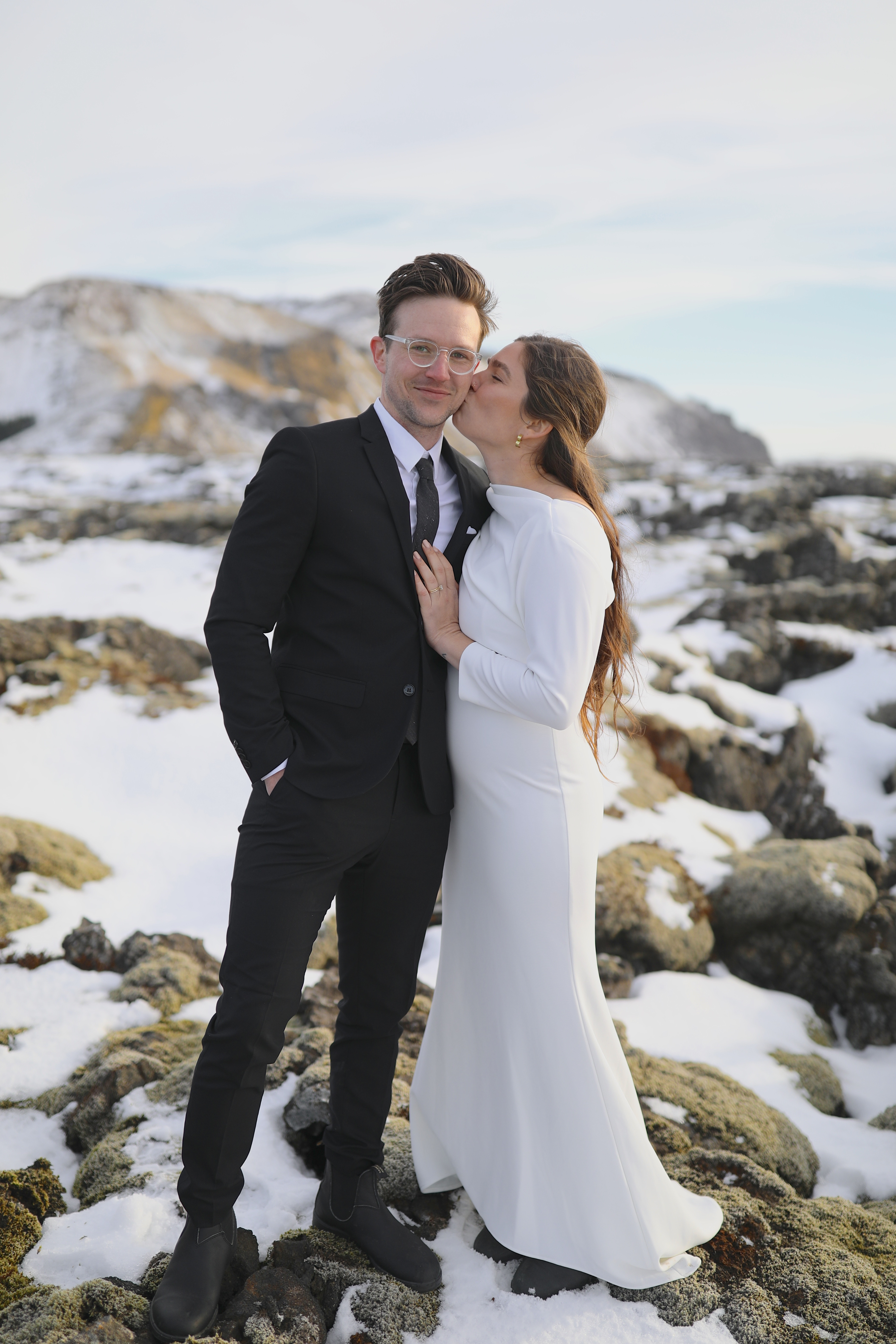 The couple posing for a wedding photo in front of a stunning Icelandic landscape, emphasizing the dramatic beauty of their well-traveled wedding location.