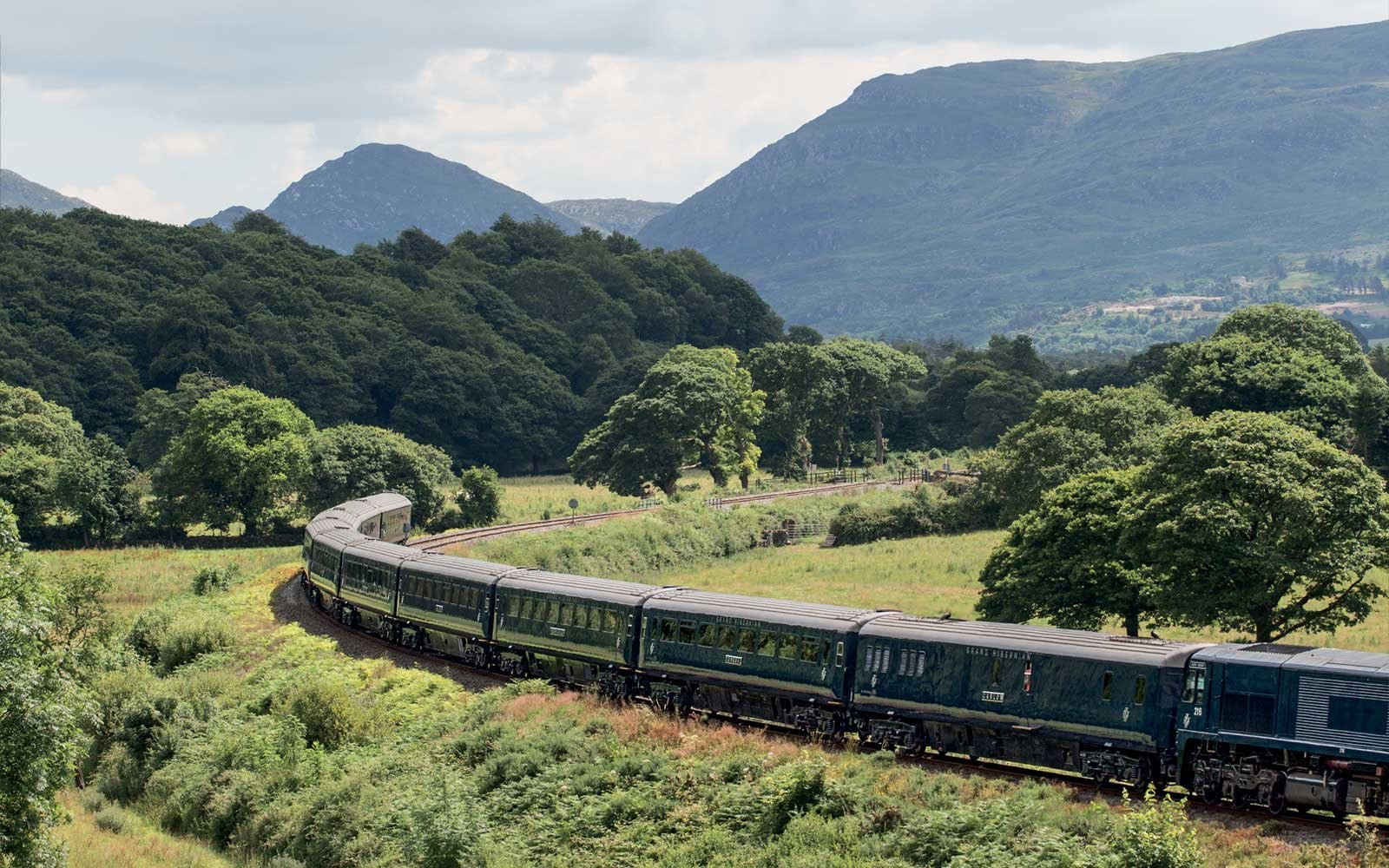 Belmond Royal Scotsman gliding through the Scottish Highlands, showcasing verdant landscapes and dramatic skies
