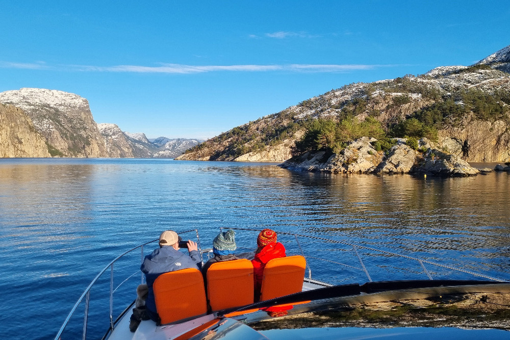 Brook and the family sitting on orange chairs on a private yacht, overlooking the Lysefjord and the mountains.