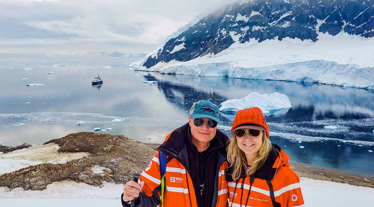 A couple enjoying the scenery in Neko Harbour, Antarctica, with icebergs and mountains in the background, representing the stunning landscapes of wilderness travel.
