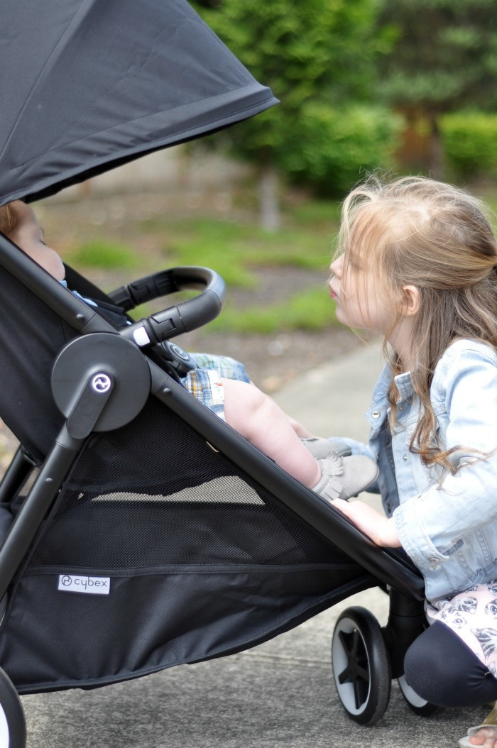 Mother demonstrating the Cybex Agis stroller's compact fold with one hand