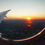 The wing of an airliner and a sunset over an urban landscape are visible from a window seat. Alt text: Airplane wing silhouetted against a vibrant sunset, symbolizing travel industry job opportunities.