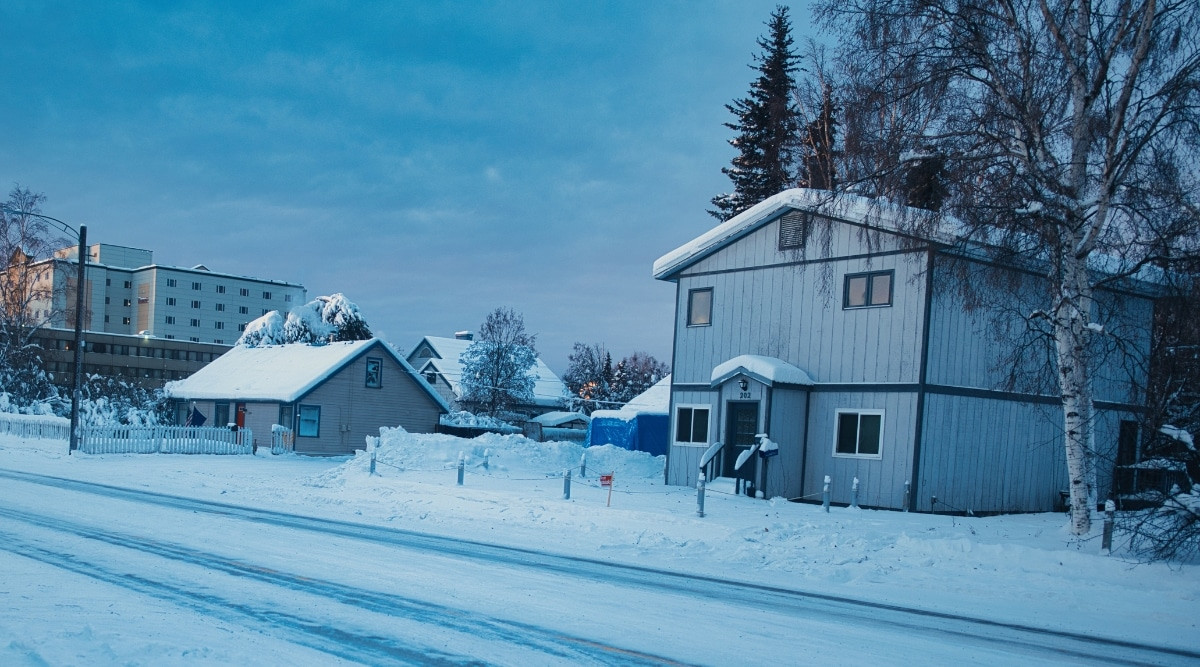 Evening view of a snow-covered city street in Fairbanks, Alaska, with snowy houses and subdued lighting.