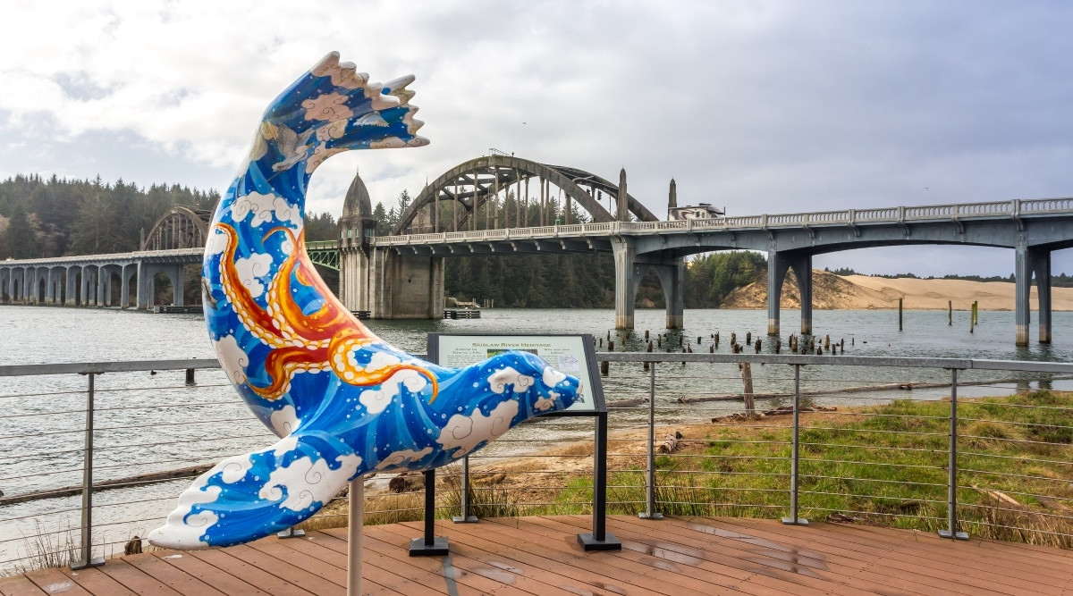 Florence, Oregon bridge with a blue seal statue in the foreground, under a cloudy sky.