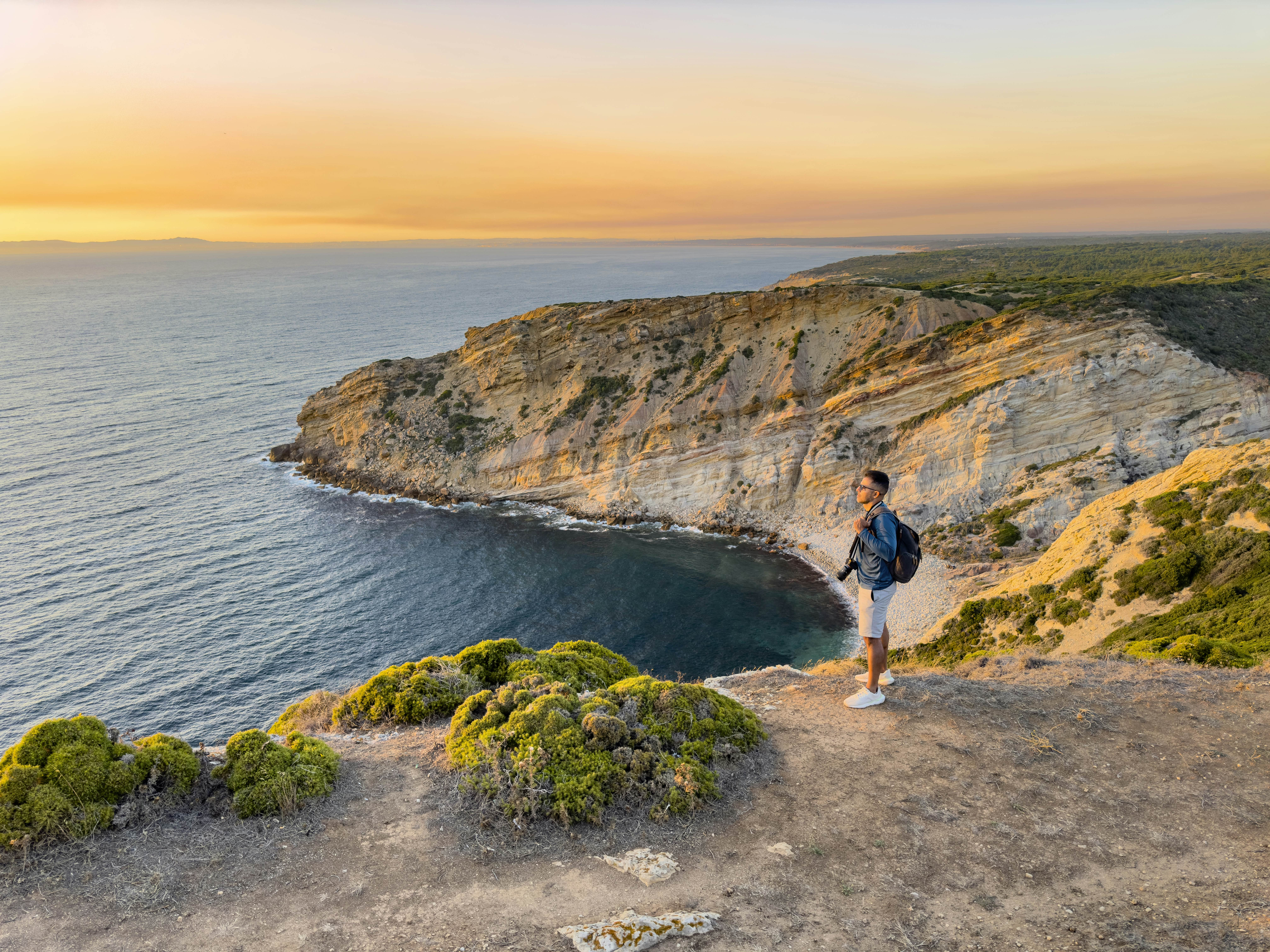 A person with a camera overlooking a sunset beach in Setúbal, Portugal