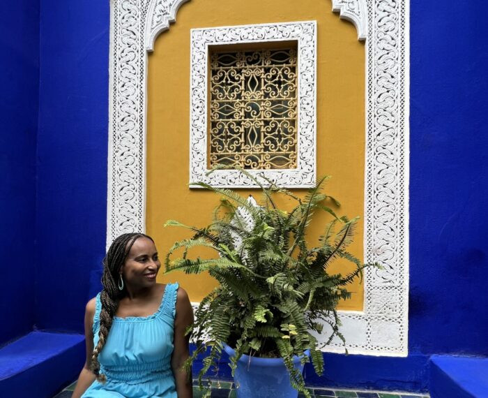 Nadeen posing in the vibrant Jardin Majorelle in Marrakech, surrounded by lush greenery and blue accents