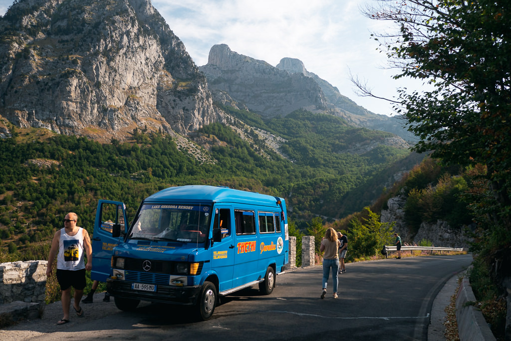 Road scene in Albania with a blue car and mountains in the distance, illustrating safe travel