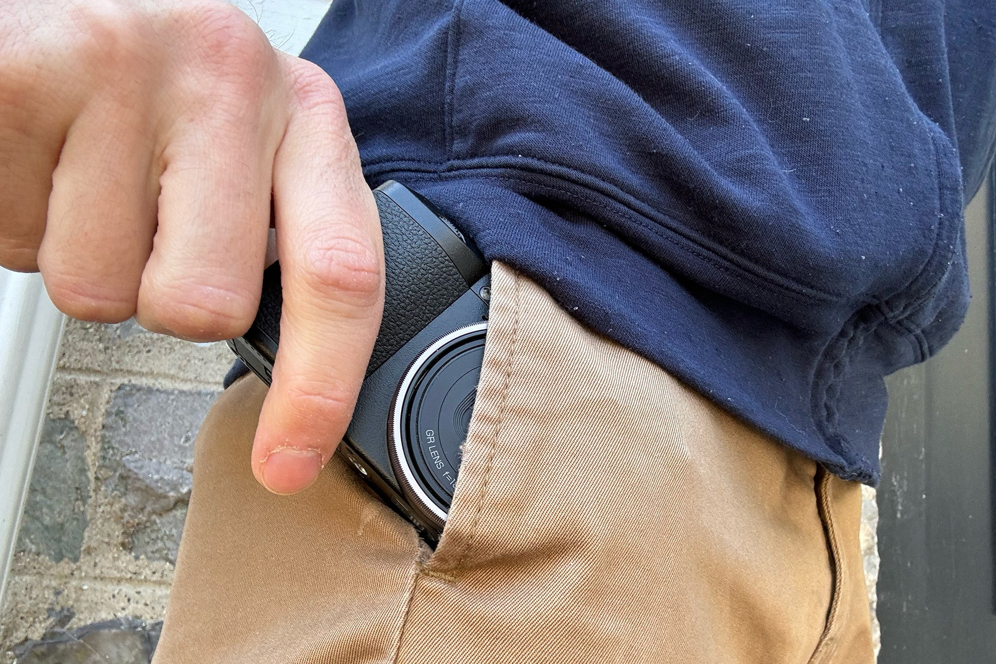 A person easily slipping the compact Ricoh GR III into their pocket, demonstrating its ultimate portability for travel