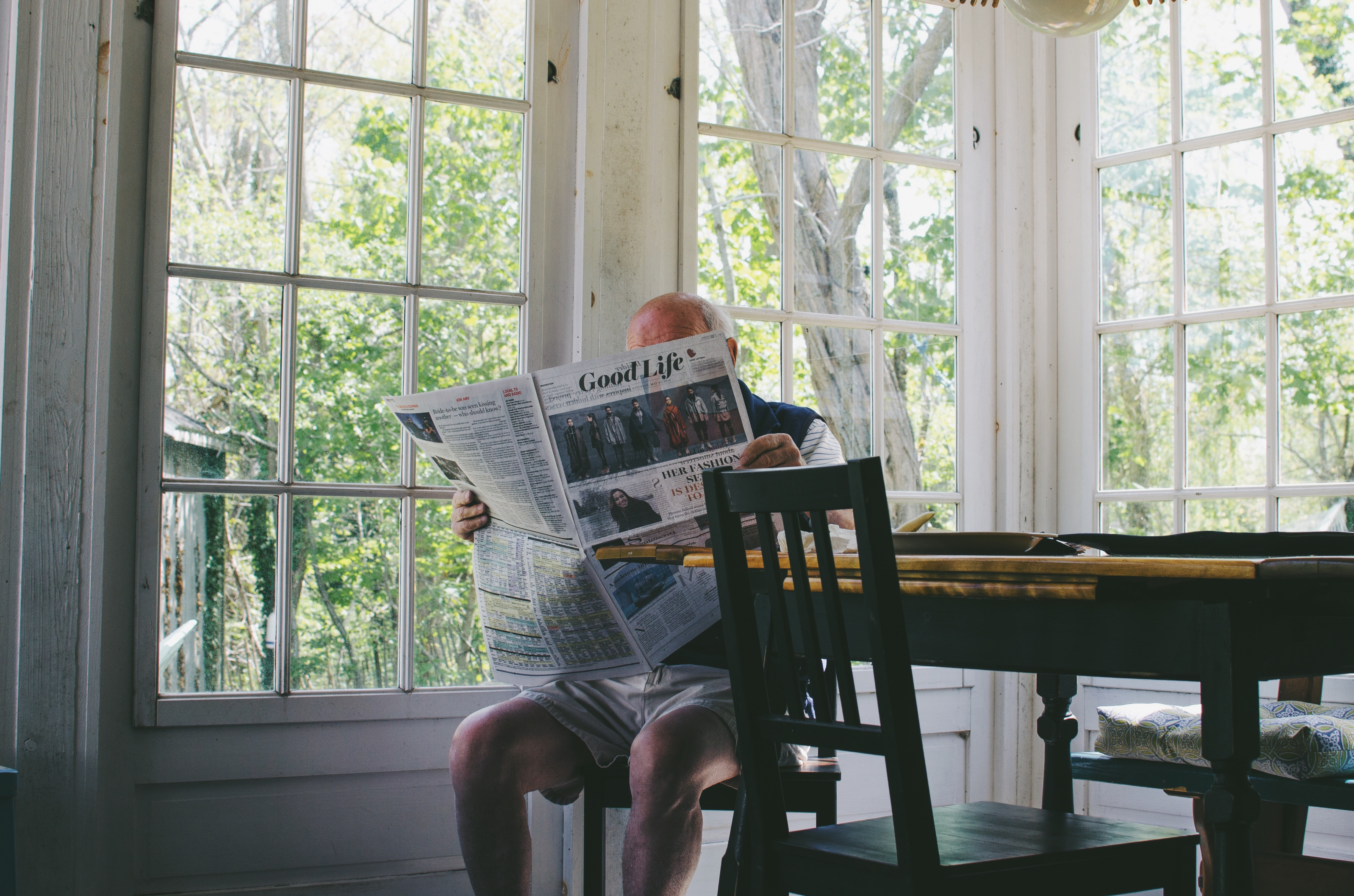 A person sitting at a table with a laptop and notebooks, seemingly working on writing, with a cup of coffee and a magazine visible, representing the work of a travel writer.