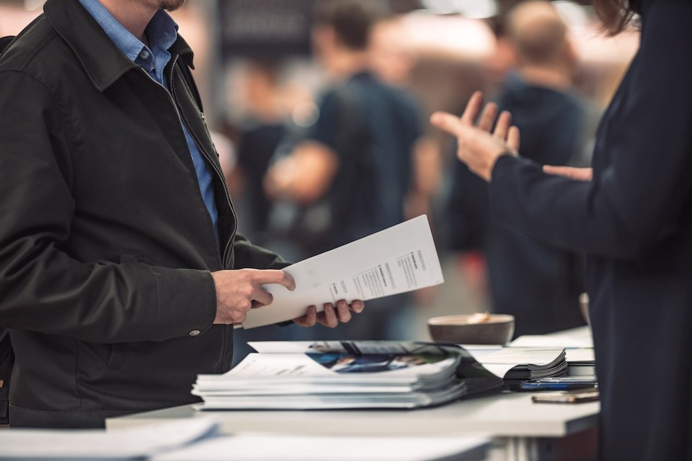 Professionals exchanging brochures and promotional materials at a bustling travel trade show.