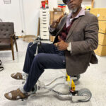 A 6'3" man demonstrates the spaciousness of the TravelScoot, a lightweight and portable travel scooter suitable for users of all sizes.