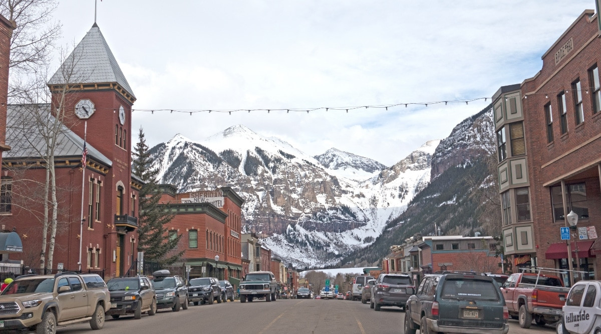 Telluride street view with snow-capped mountains in the background, under an overcast sky.