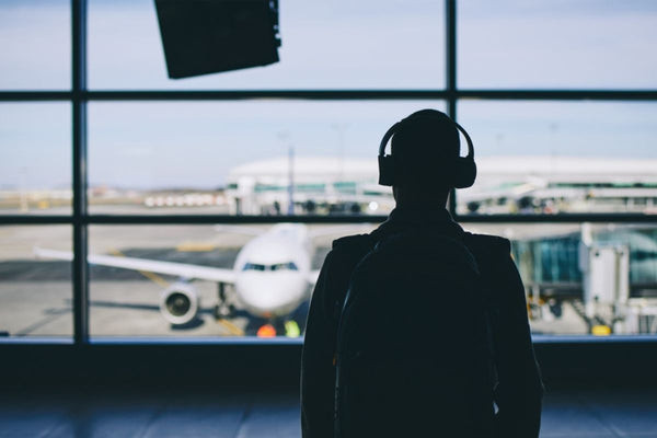A traveler in an airport uses noise cancelling headphones, highlighting practical travel gifts for her