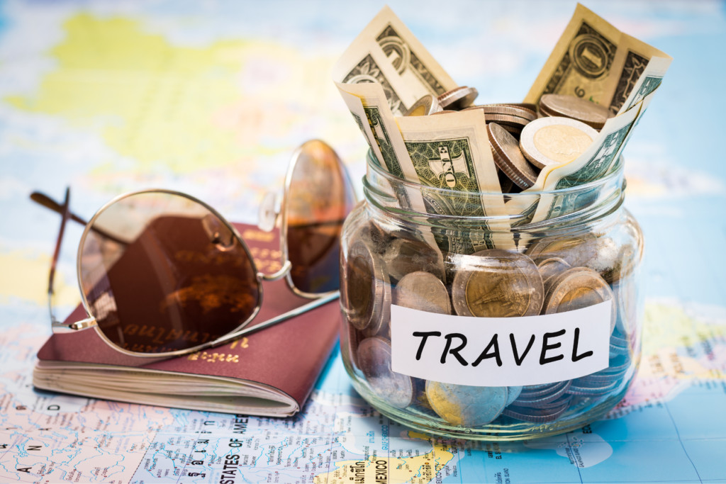 Jar of cash on world map with passport and sunglasses