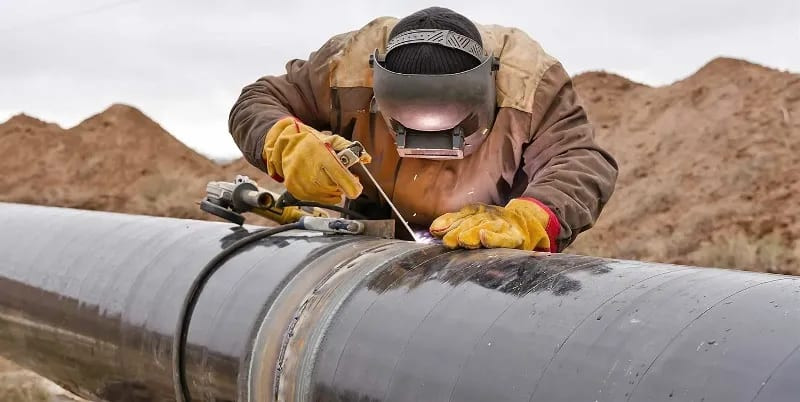 A skilled traveling welder expertly welds a metal structure outdoors, showcasing precision and expertise in their mobile work environment.