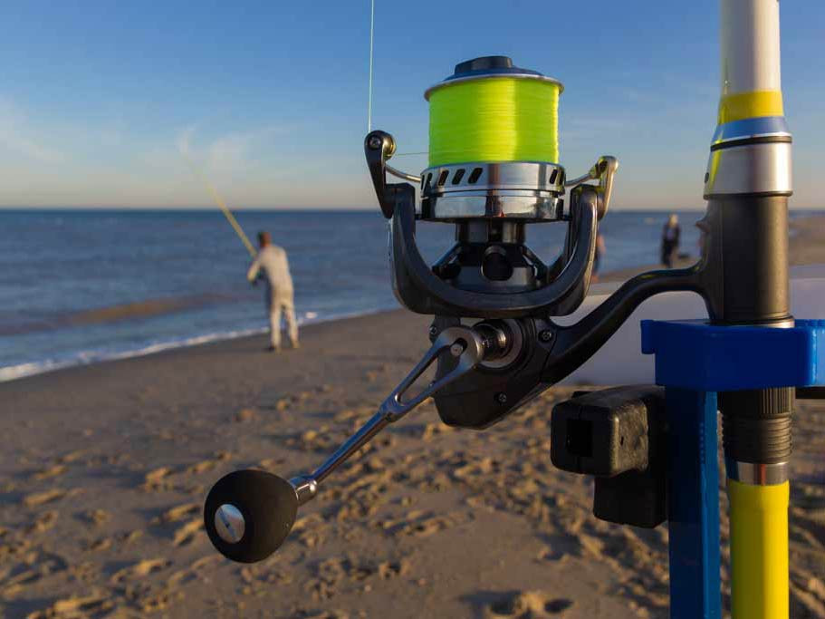 A close-up of surf fishing reels with a surf fisherman in the background, focusing on the gear used for surf fishing.