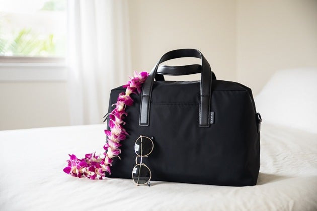 Away The Everywhere Bag on bed with sunglasses resting against the bag, a stylish and practical travel bag for your essentials.