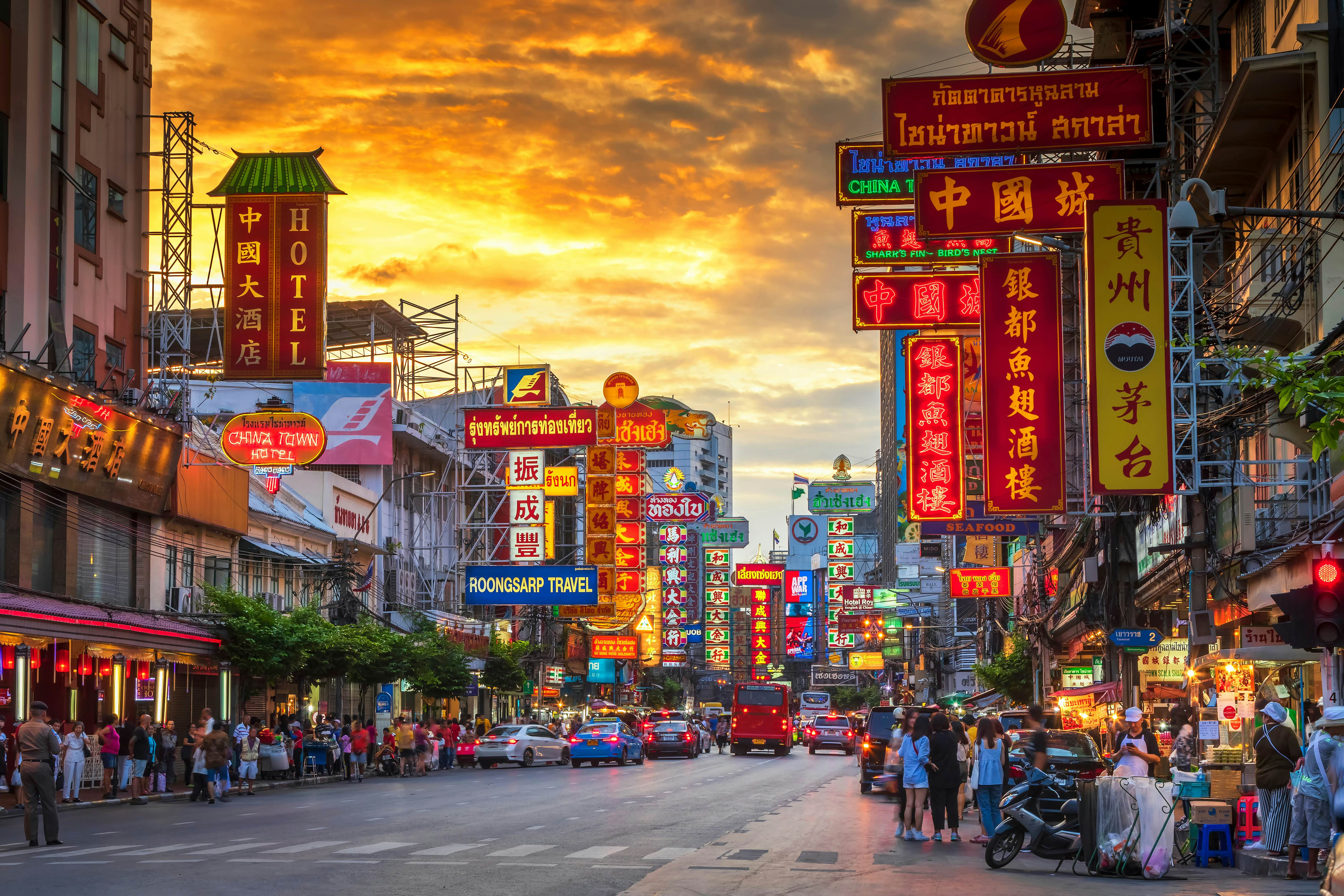 A vibrant street scene in Bangkok's Chinatown, lit up with neon signs and bustling with food stalls
