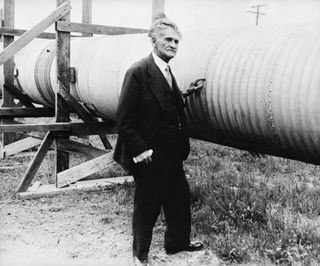 Dr. Albert A. Michelson, standing next to a long vacuum tube used for measuring light speed in 1930